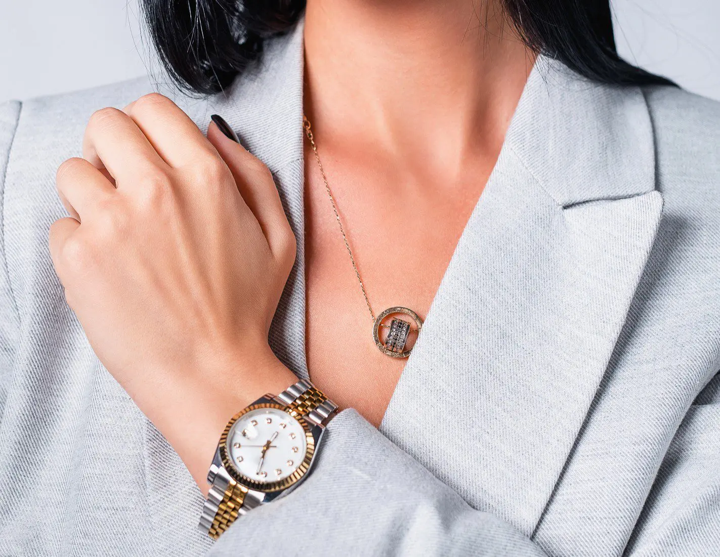 Woman wearing watch and necklace, gray blazer.