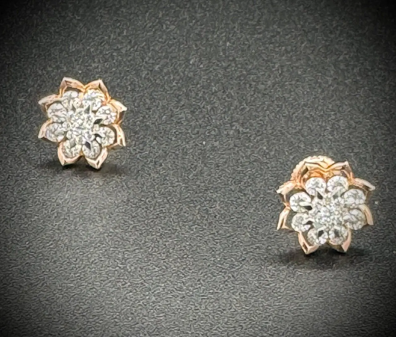 Elegant floral diamond earrings with a gold base on a dark background.