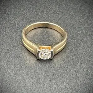 Elegant gold ring with a central diamond on a textured surface.