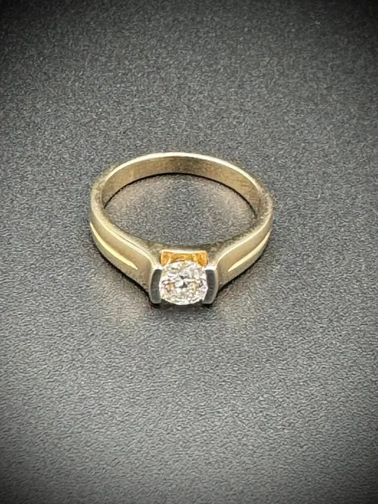 Elegant gold ring with a central diamond on a textured surface.