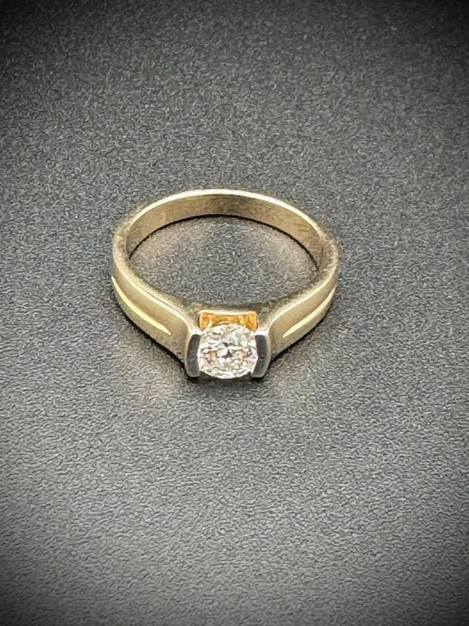 Elegant gold ring with a central diamond on a textured surface.