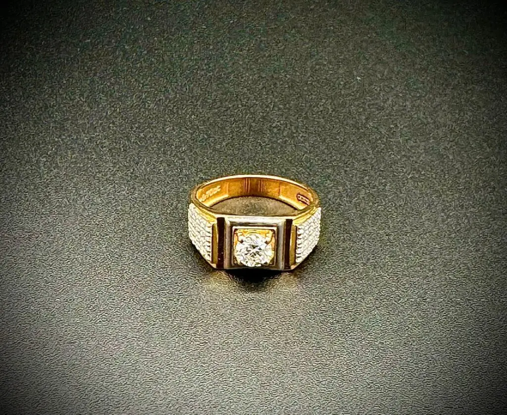 Gold ring with a central diamond on a dark textured surface.