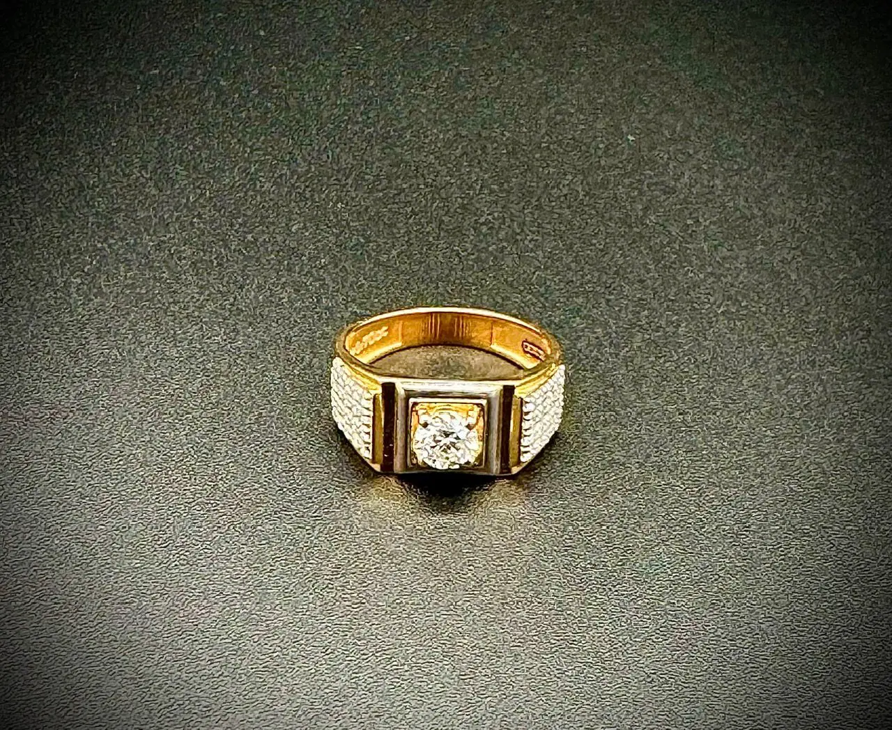 Gold ring with a central diamond on a dark textured surface.