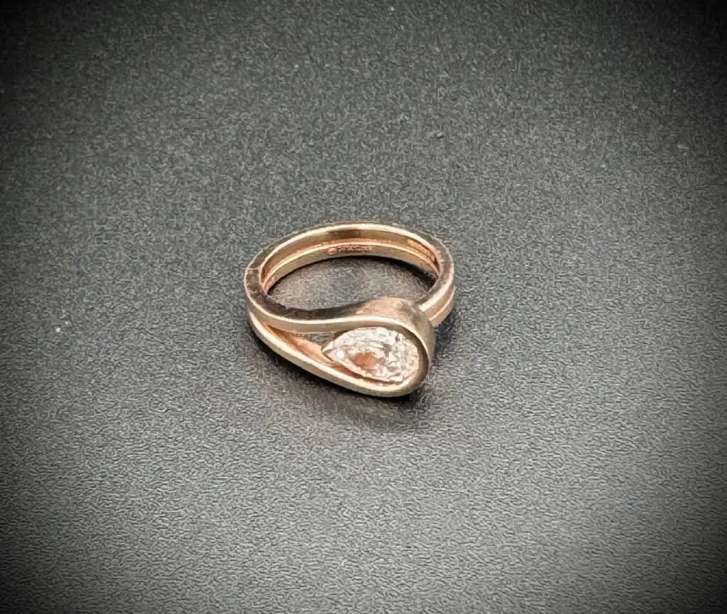 Elegant rose gold ring with a teardrop-shaped design and central gem.