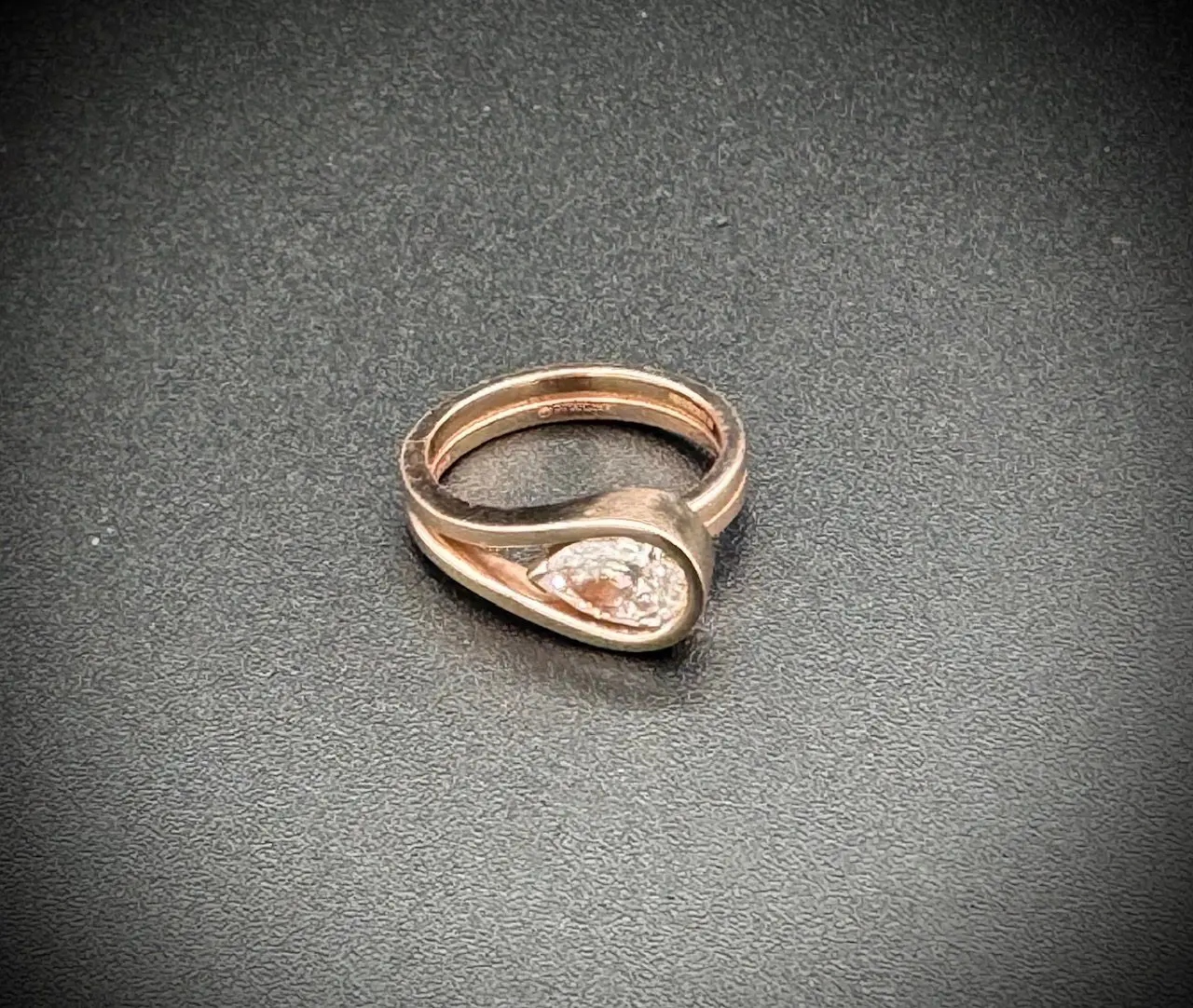 Elegant rose gold ring with a teardrop-shaped design and central gem.